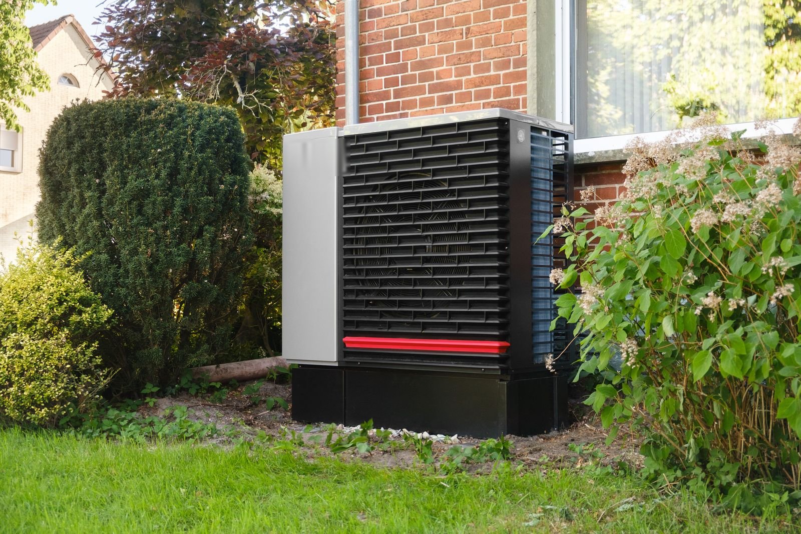 Wärmepumpe im Garten vor einem Backsteinhaus